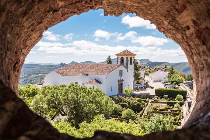 Historic village of Marvão seen through a stone arch, with whitewashed buildings and mountain views.