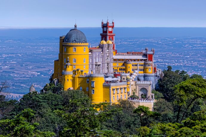 Colorful Pena Palace perched on a hilltop in Sintra, Portugal, surrounded by lush forest.