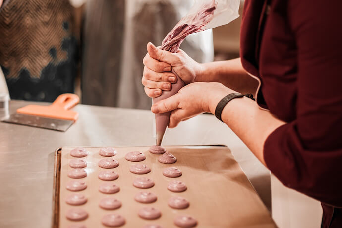 Pastry chef piping purple macaron batter onto a tray