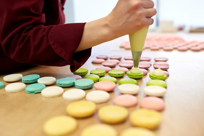 Hand placing vibrant macarons on a tray in a pastry shop