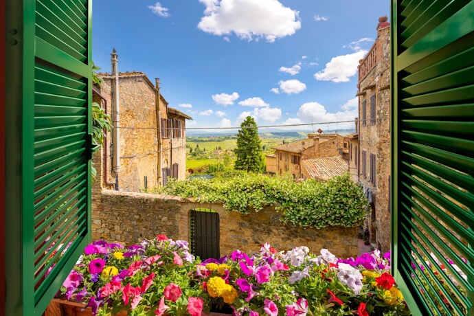 A flower-framed view of rolling hills from a village window, in Italy.