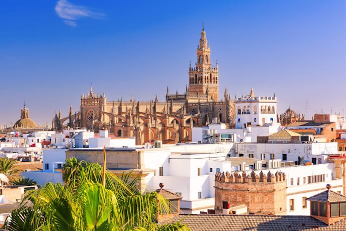 Panoramic view of Seville’s historic center with the Cathedral and Giralda tower rising above white rooftops under a clear blue sky.
