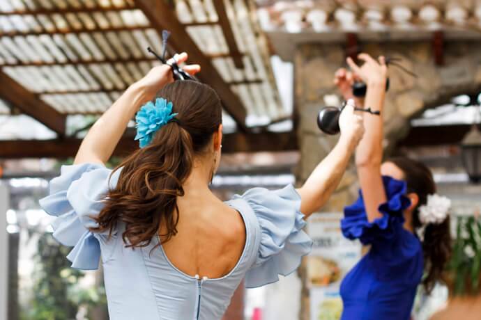 Two flamenco dancers performing in Seville with colorful dresses and arms raised in traditional Spanish dance pose.