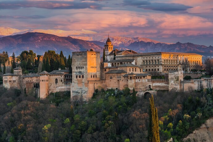 Golden sunset view of the Alhambra in Granada with the Sierra Nevada mountains in the background.