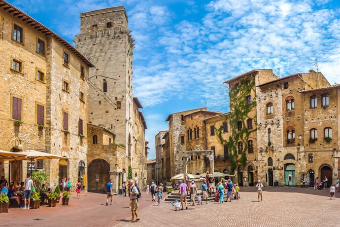 People in Piazza della Cisterna in San Gimignano, featuring stone buildings and tower houses