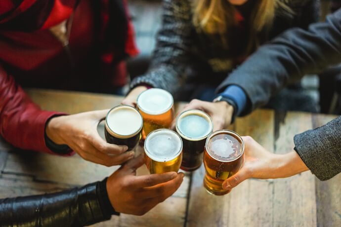 Close-up of friends clinking glasses of beer over a rustic wooden table, with different types of beers 