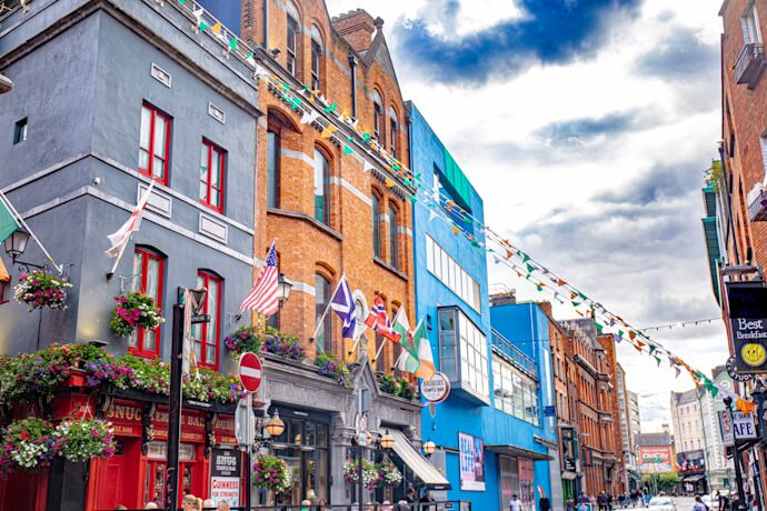 Colorful street scene in Dublin’s Temple Bar district, with historic brick buildings, hanging flower baskets, flags, and pedestrians enjoying the vibrant atmosphere.
