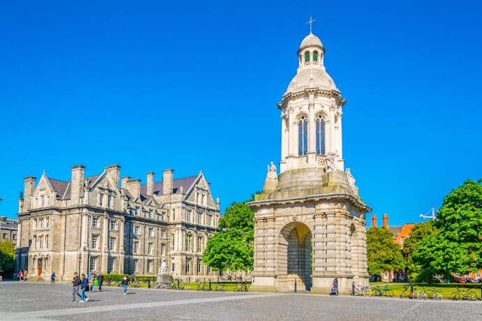Stone bell tower (Campanile) at Trinity College Dublin, standing in a spacious cobbled courtyard surrounded by historic university buildings
