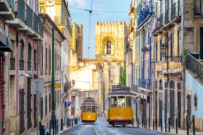 Street in Lisbon and yellow trams with the Gothic Sé de Lisboa on the background