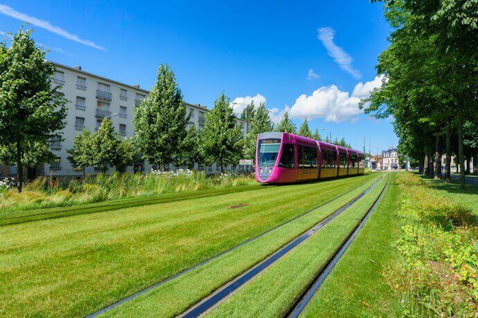 A pink tram glides along a lush green track in the picturesque city of Reims