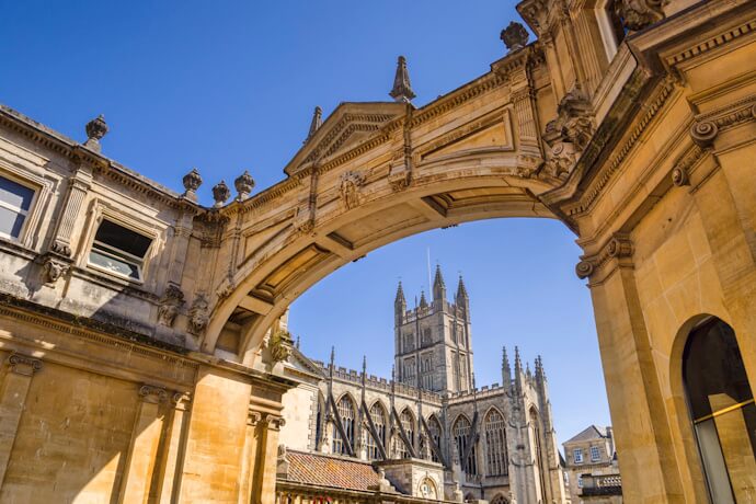 View of Bath Abbey through a historic stone archway, highlighting Gothic architecture