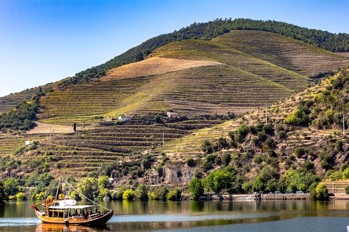 Traditional rabelo boat sailing along the terraced vineyards of the Douro Valley, Portugal