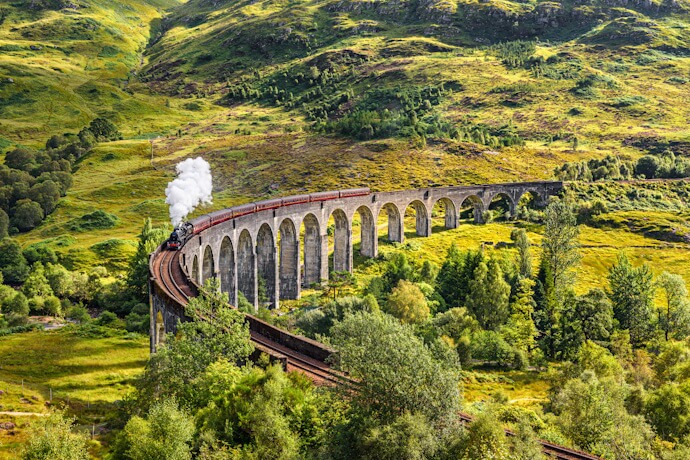 Train crossing the Glenfinnan Viaduct in the Scottish Highlands, surrounded by dramatic green landscapes