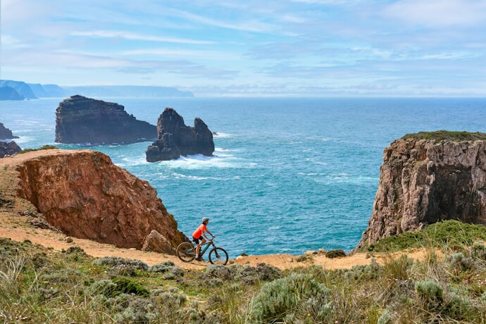 Cyclist overlooking dramatic coastal cliffs near Sagres, Algarve.