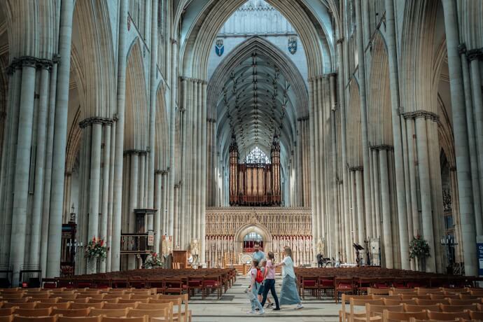Visitors walking inside York Minster in England, admiring the soaring Gothic arches and stained-glass windows
