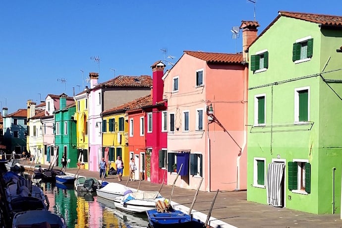 Colorful houses along a canal with boats in Burano, Italy, on a sunny day.