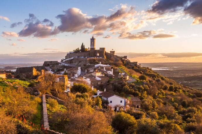 Golden light bathes Monsaraz, in the Alentejo, revealing its hilltop castle, whitewashed houses, and vast plains stretching into the distance.