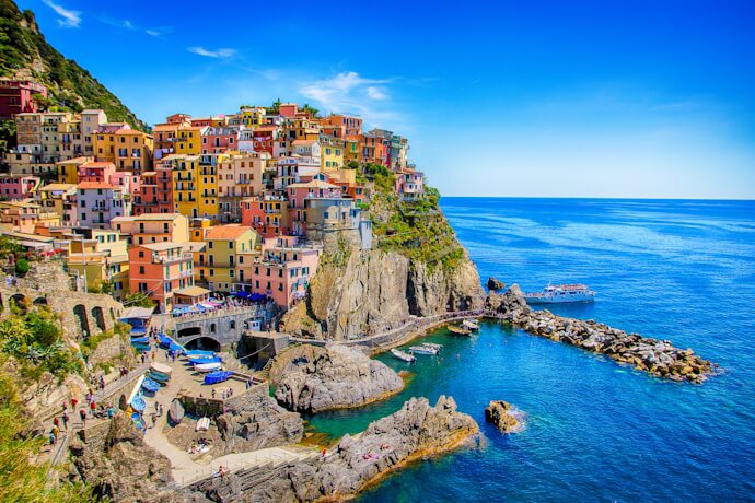 Iconic pastel buildings in Manarola, cascading down rocky cliffs toward a small harbor and crystal-clear waters.