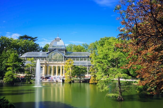 The Crystal Palace in Madrid’s El Retiro Park, reflected in a peaceful pond with a water fountain and surrounded by lush tree